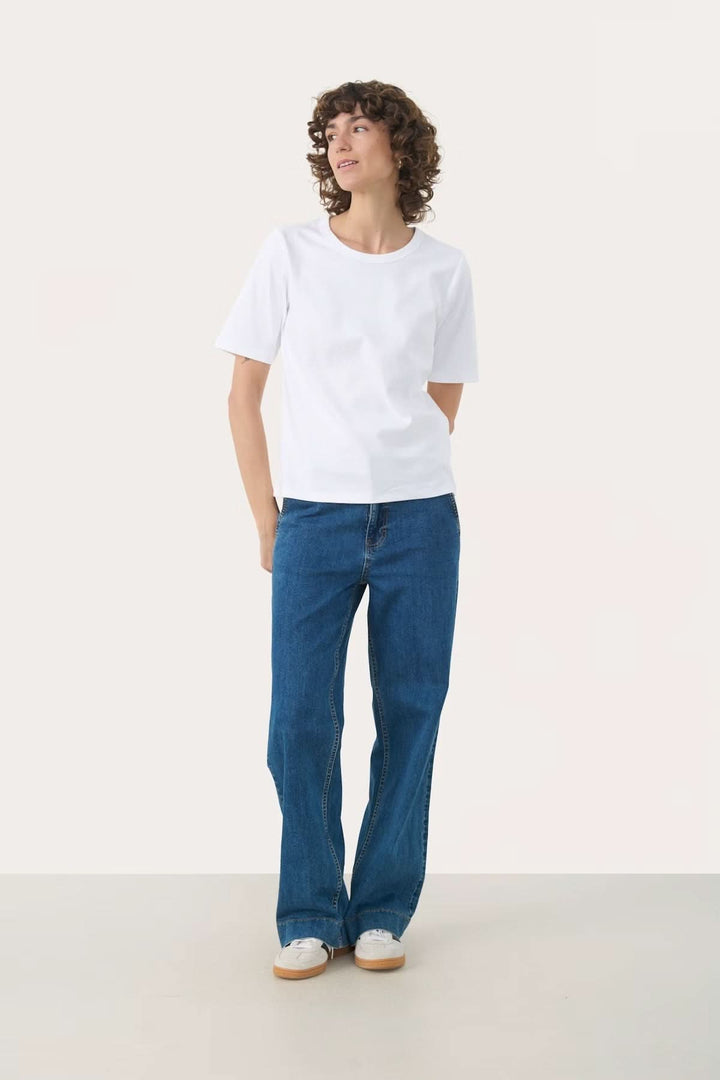Femme portant un t-shirt blanc à col rond avec un jean bleu, style décontracté et moderne.