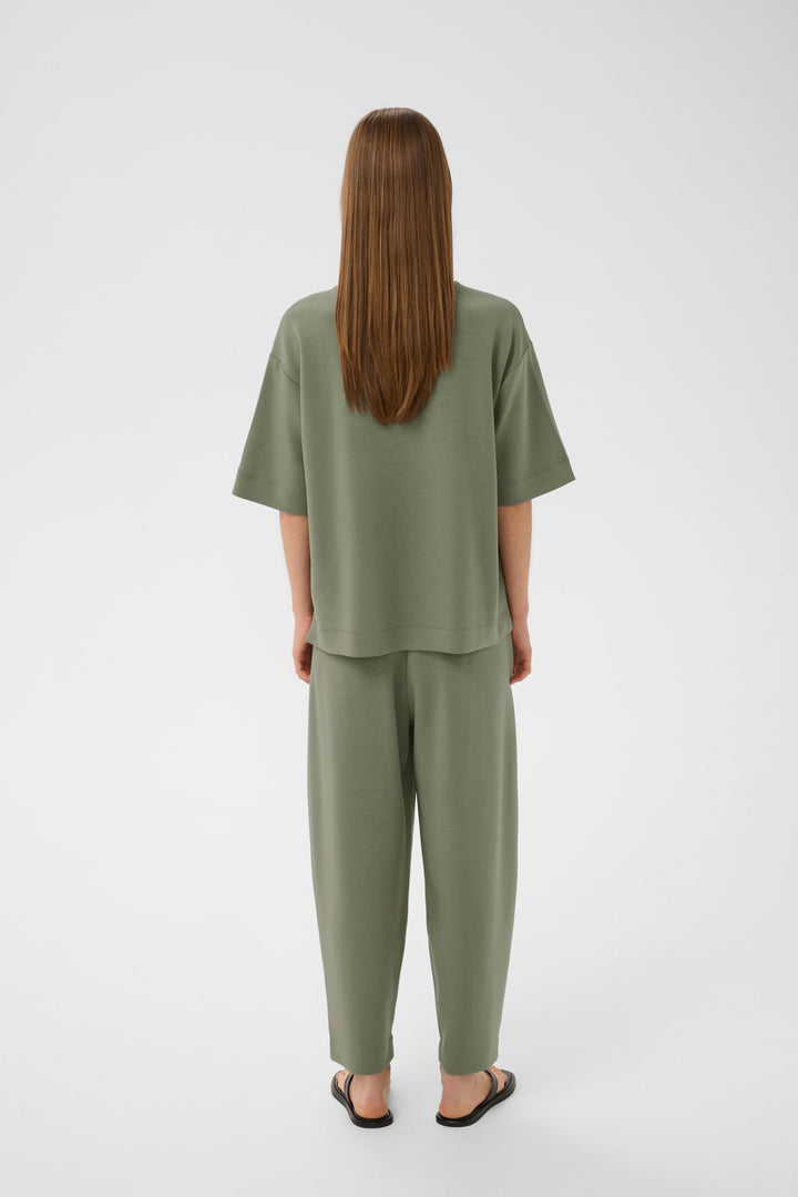 Vue arrière du T-shirt coupe ample Pannie vert avec manches courtes, porté avec un pantalon coordonné et des sandales noires.
