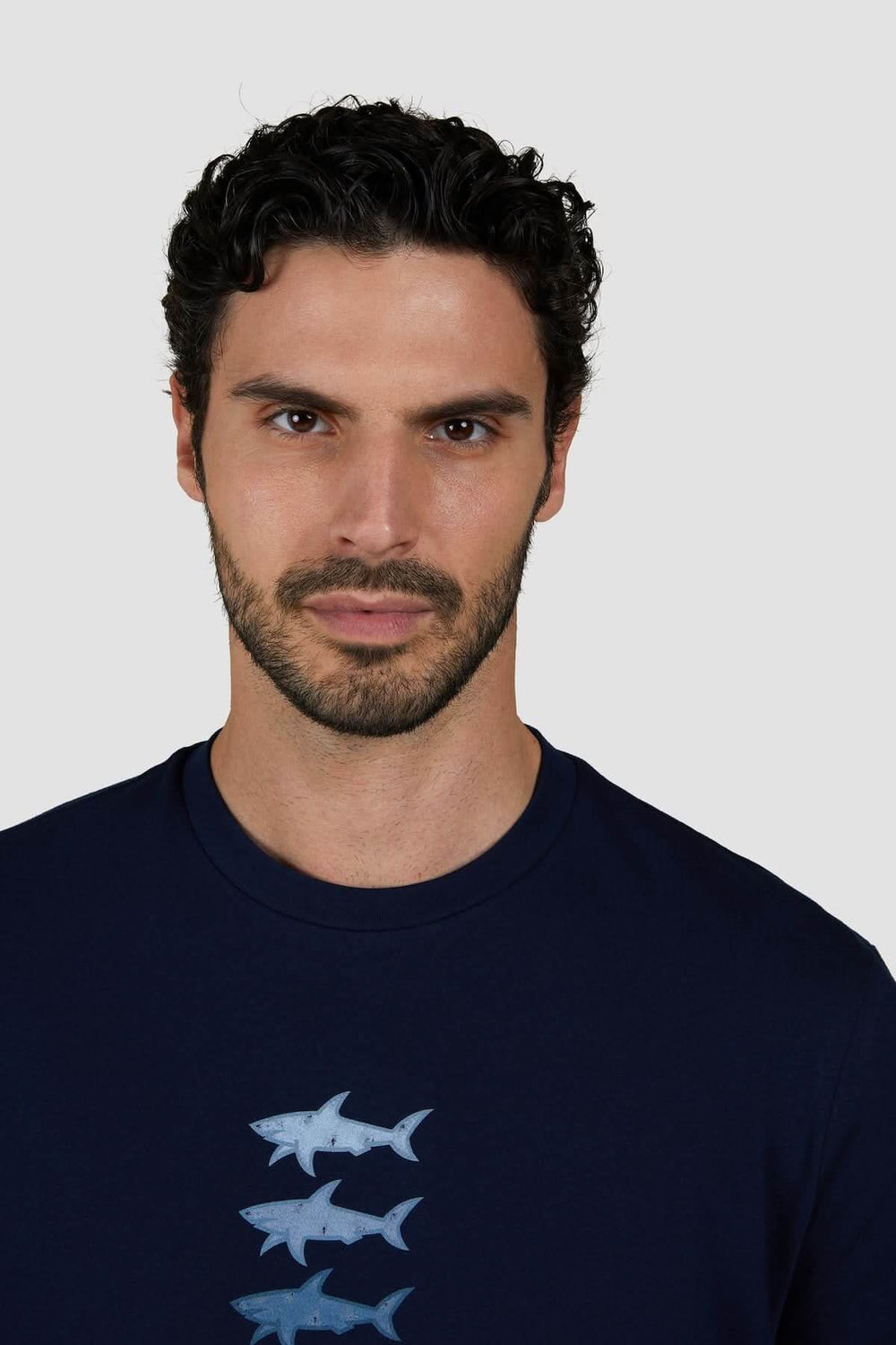Homme portant un t-shirt en coton bleu marine avec imprimé de trois requins stylisés sur la poitrine.