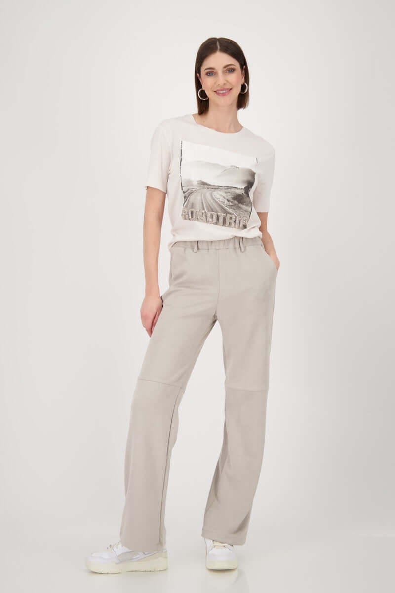 Femme portant un t-shirt imprimé photo 'road trip' avec un pantalon beige et des chaussures blanches.