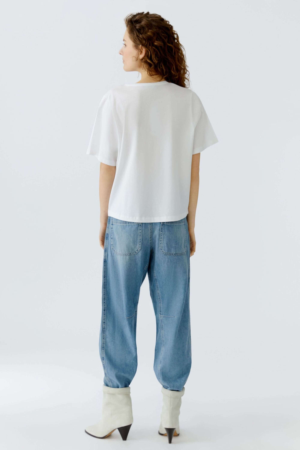 Personne portant un t-shirt imprimé graphique et un jean, vue de dos, avec des manches courtes et coupe décontractée.