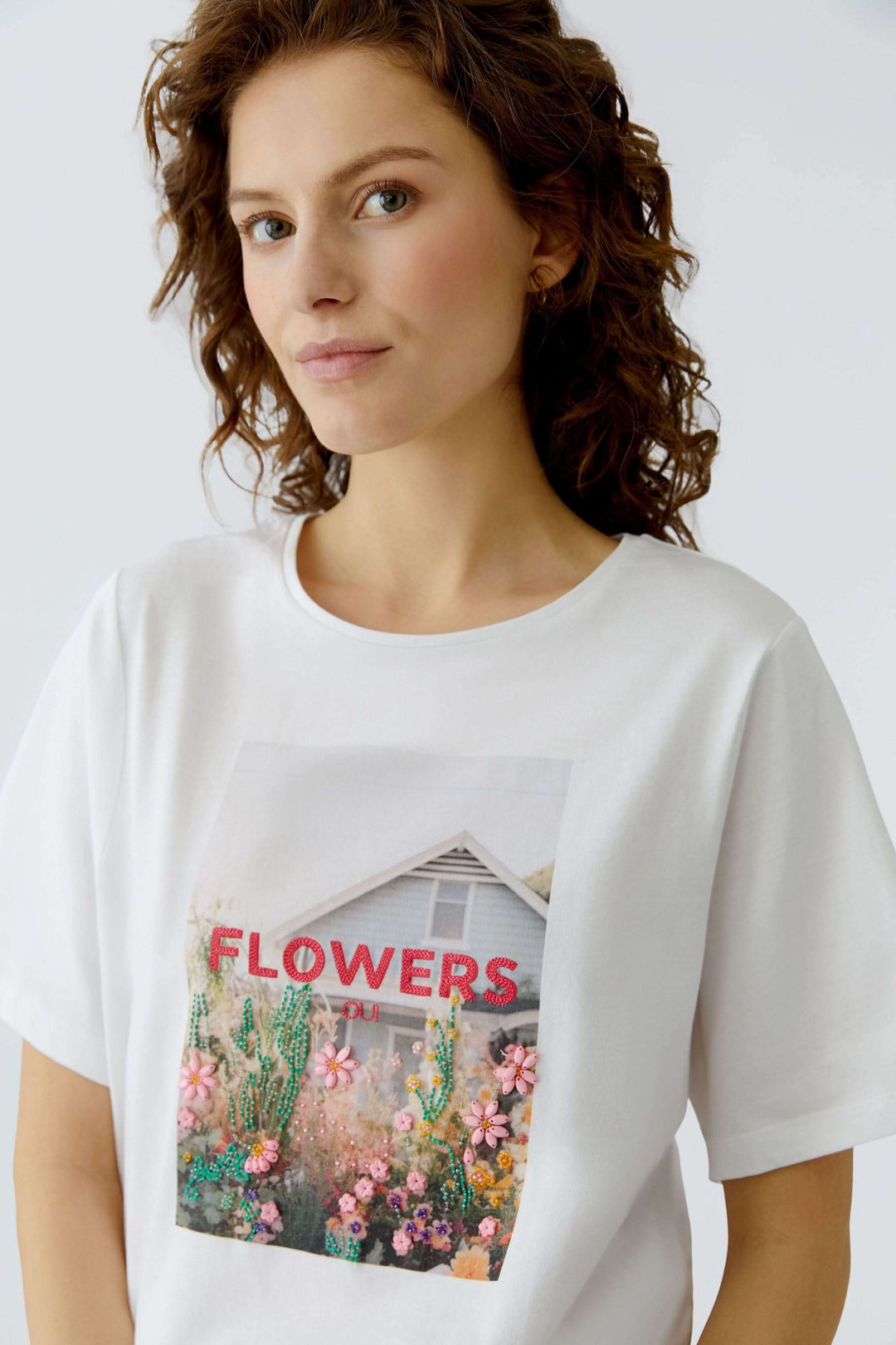 Femme portant un T-shirt imprimé graphique avec motif floral et texte "FLOWERS", coupe droite et manches courtes.