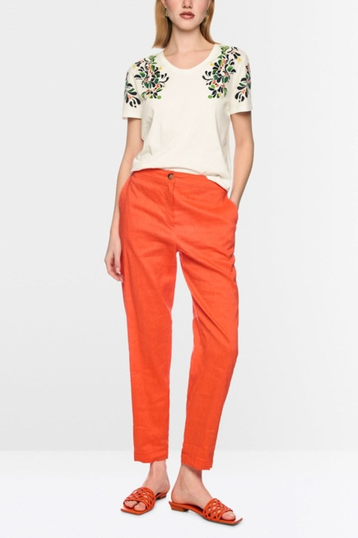 Modèle portant un t-shirt imprimé hibiscus et paillettes, manches courtes, col rond, avec perles, sur un pantalon orange vif.