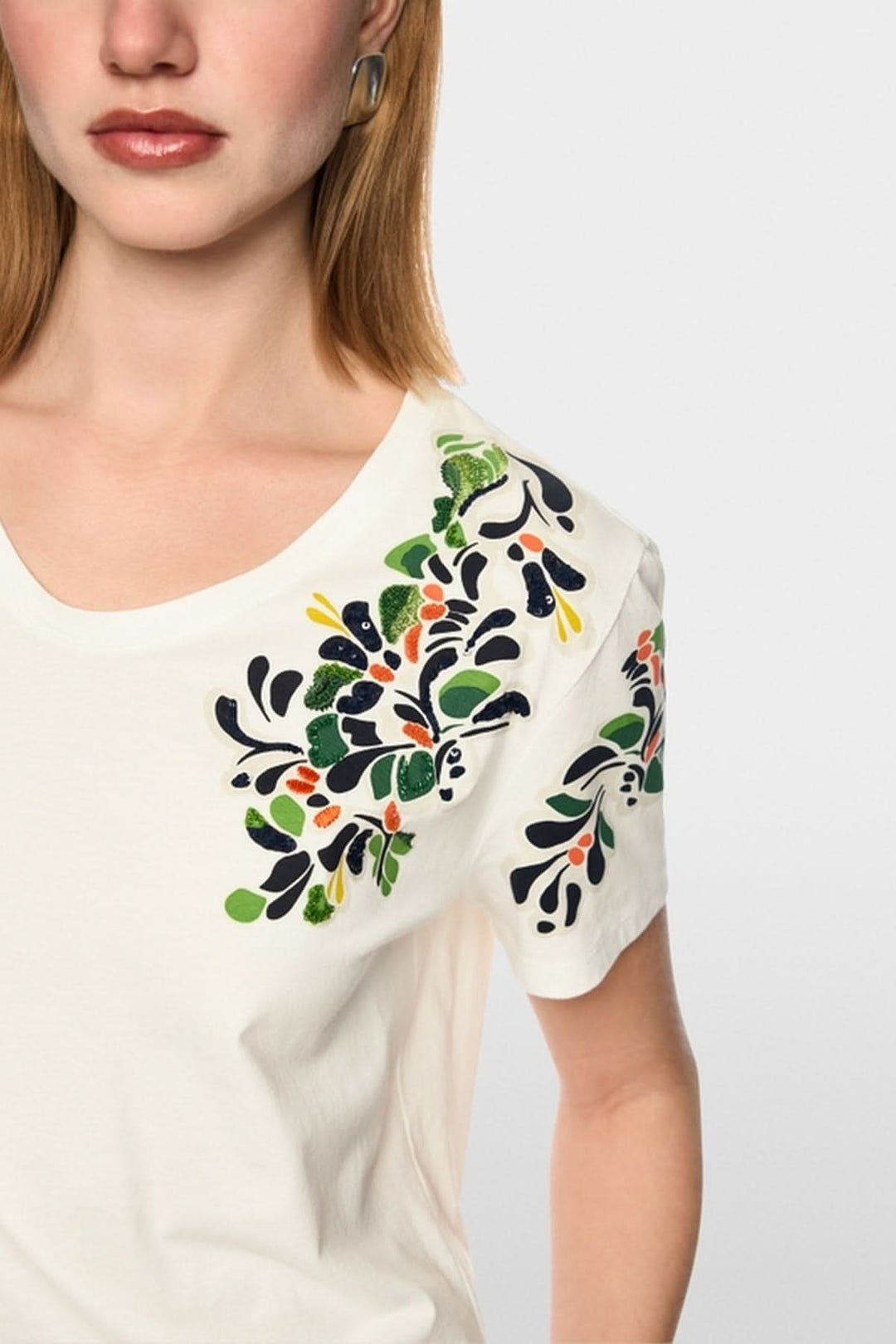 T-shirt imprimé hibiscus et paillettes en coton, avec manches courtes et détails floraux colorés, porté par un mannequin.