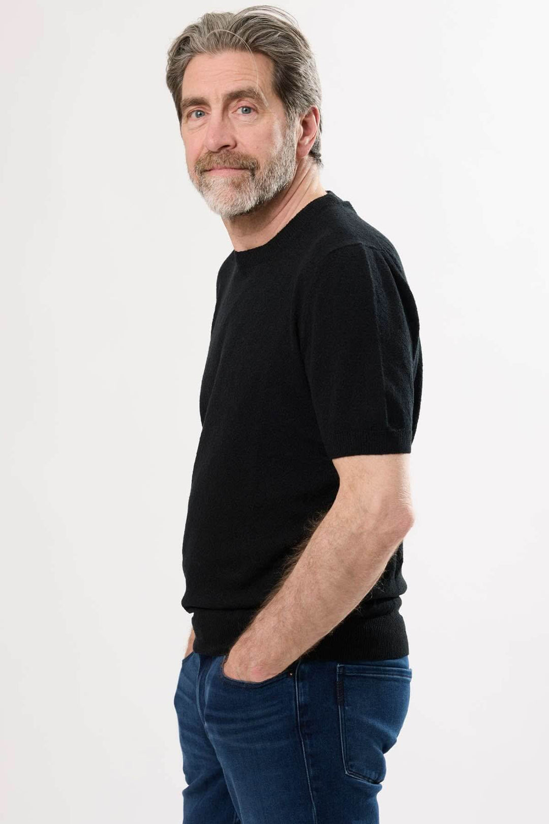 Homme souriant en t-shirt noir, style décontracté, pose de profil, fond blanc.