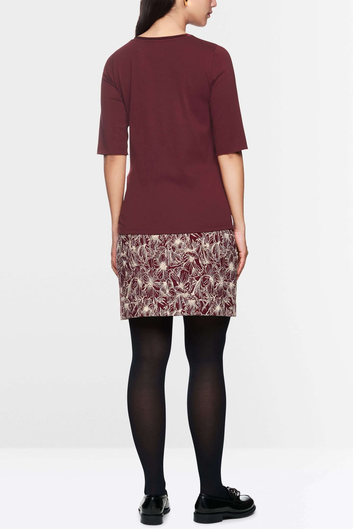 Femme vue de dos avec un t-shirt manches courtes et une jupe à motifs, style classique et élégant.