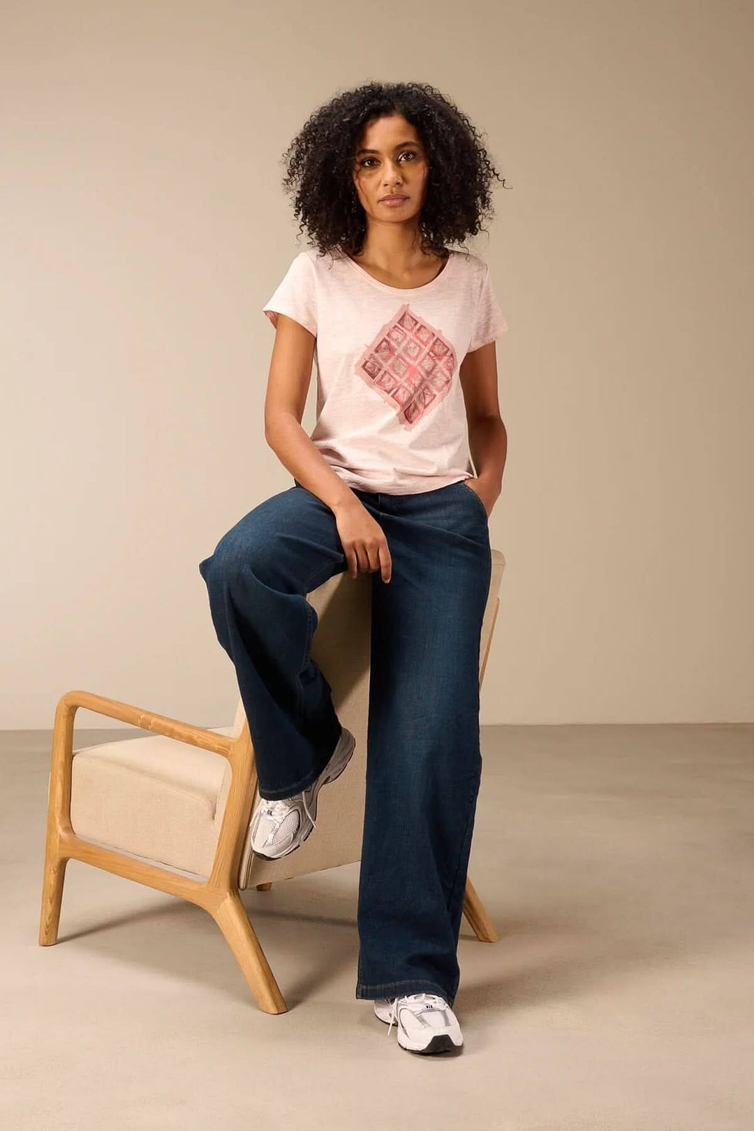 Femme portant un t-shirt à manches courtes coupe décontractée, assise sur une chaise, vêtue d&