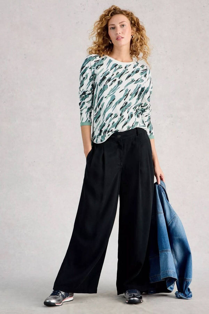 Femme portant un T-shirt à manches longues Clara avec pantalon ample noir, tenant une veste en jean.