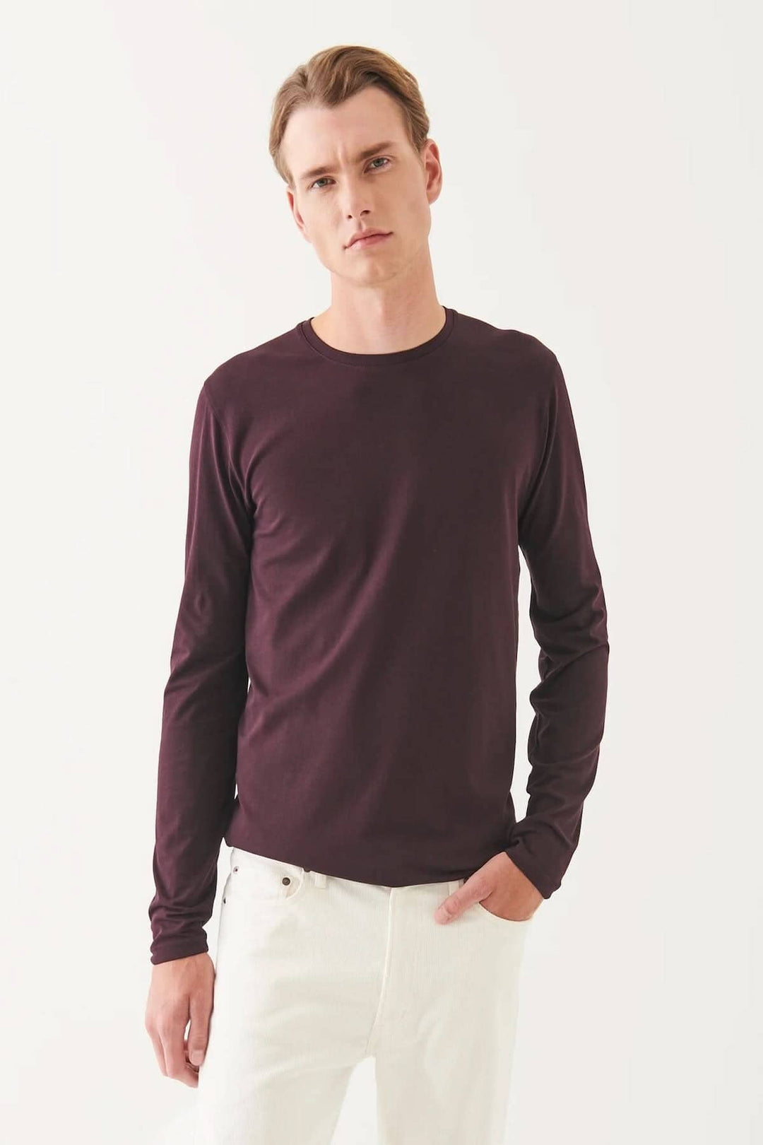 Homme portant un t-shirt manches longues en coton Pima péruvien, couleur bordeaux, avec pantalons blancs.