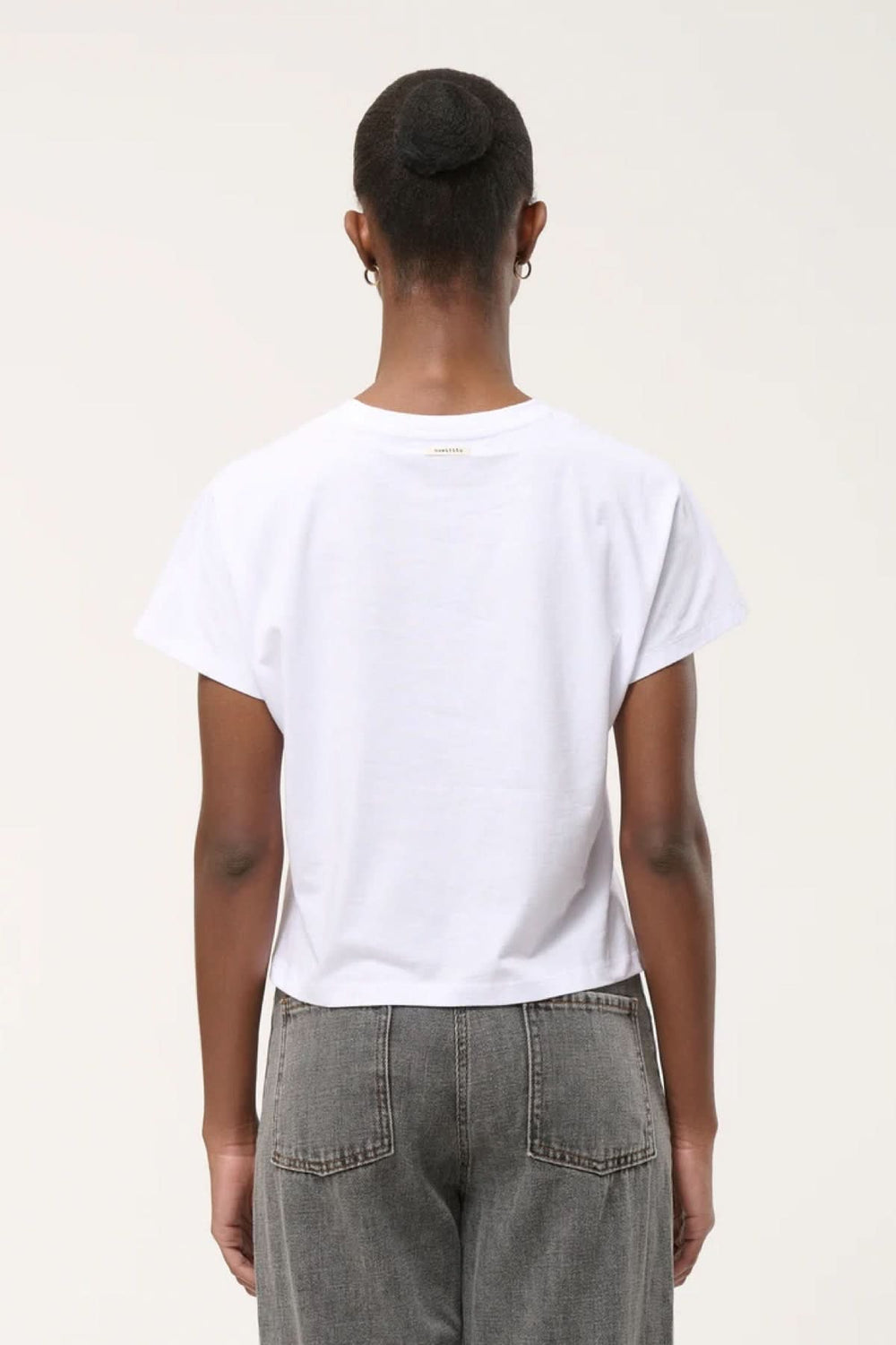 Vue arrière d'un T-shirt à ourlet asymétrique en coton blanc porté par une femme, mettant en valeur la coupe simple et épurée.