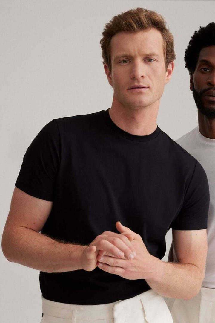 Homme en t-shirt noir à coupe moderne, regard confiant, avec un autre homme en arrière-plan.