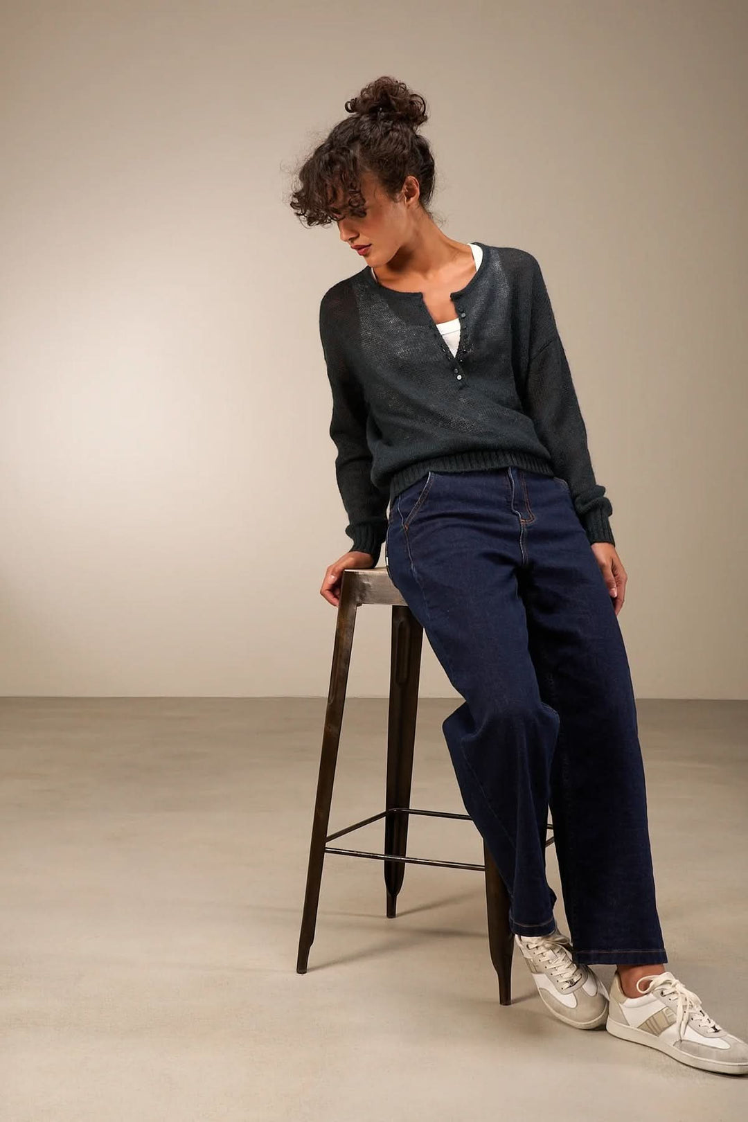 Femme portant un tricot doux à patte de boutonnage décorative avec un denim taille haute, créant un look décontracté et automnal.