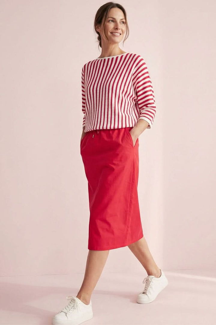 Femme portant un tricot rayé manches trois-quarts avec une jupe rouge, look décontracté et élégant, décrit moi le produit en français.