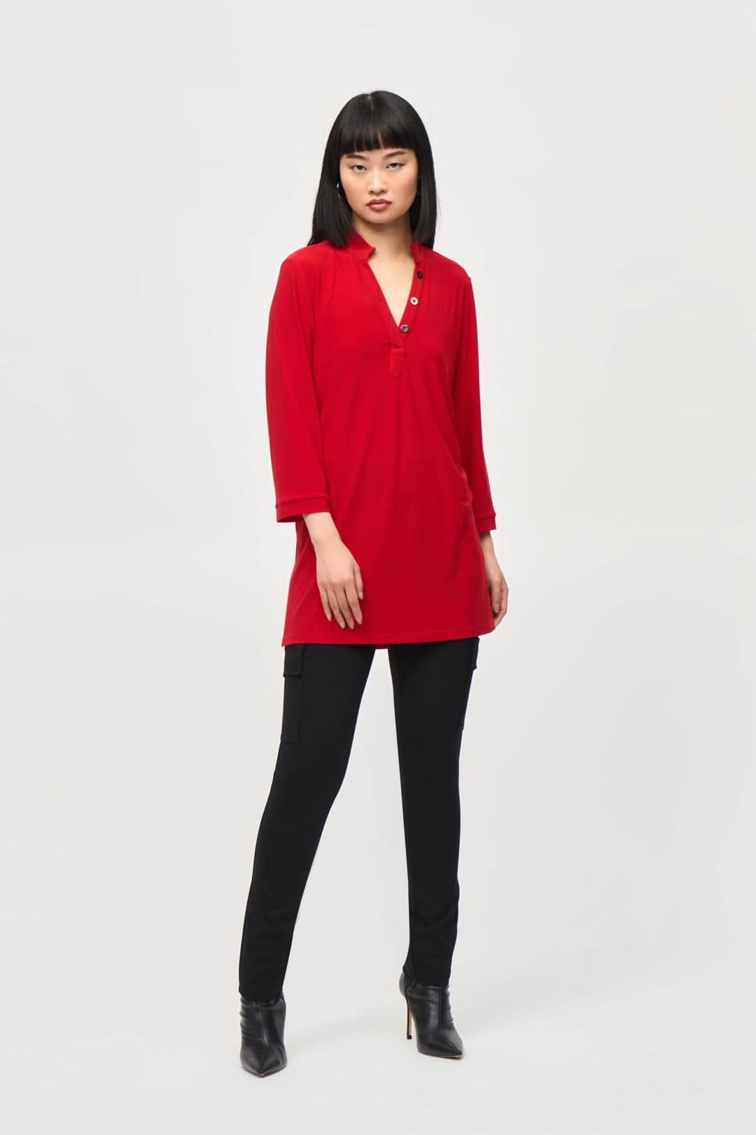 Tunique rouge encolure en V avec patte de boutonnage et manches 3/4, portée avec un pantalon noir.