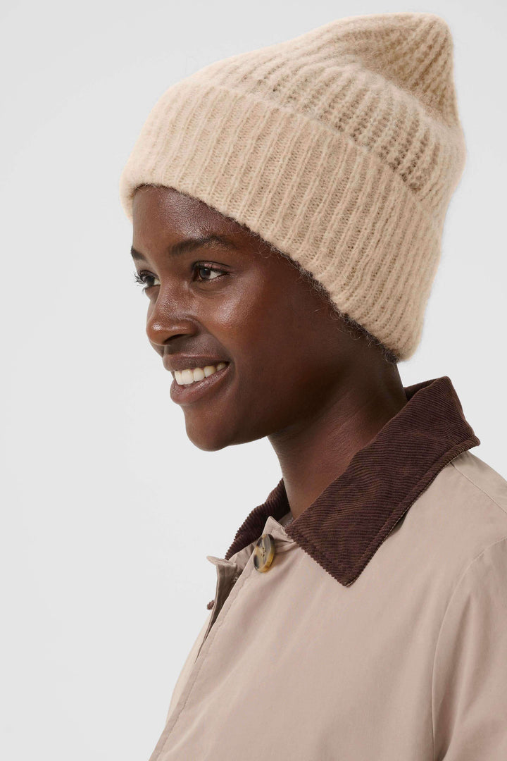 Person wearing Tuque Sanja en tricot côtelé beige, coupe moderne et effet décontracté, idéale pour un style urbain doux et chaud.