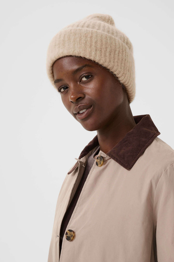 Modèle portant une tuque Sanja en tricot côtelé beige, style moderne et décontracté pour un look hivernal urbain.