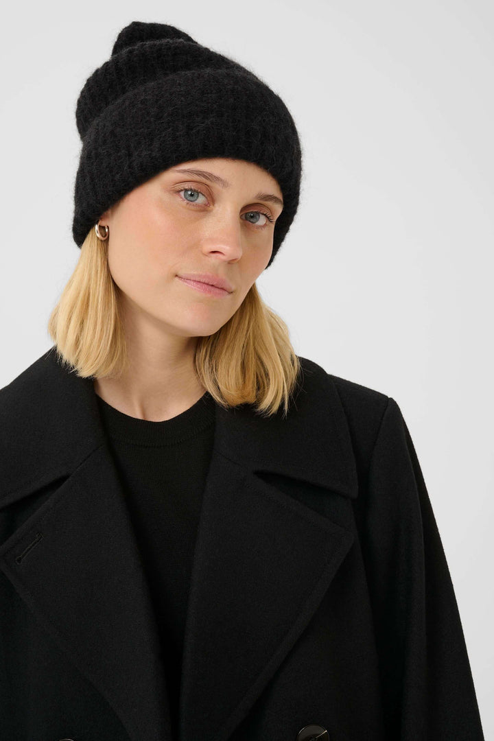 Femme portant la tuque Sanja en tricot côtelé noir, style moderne et décontracté, idéal pour un look d'hiver urbain et chaleureux.