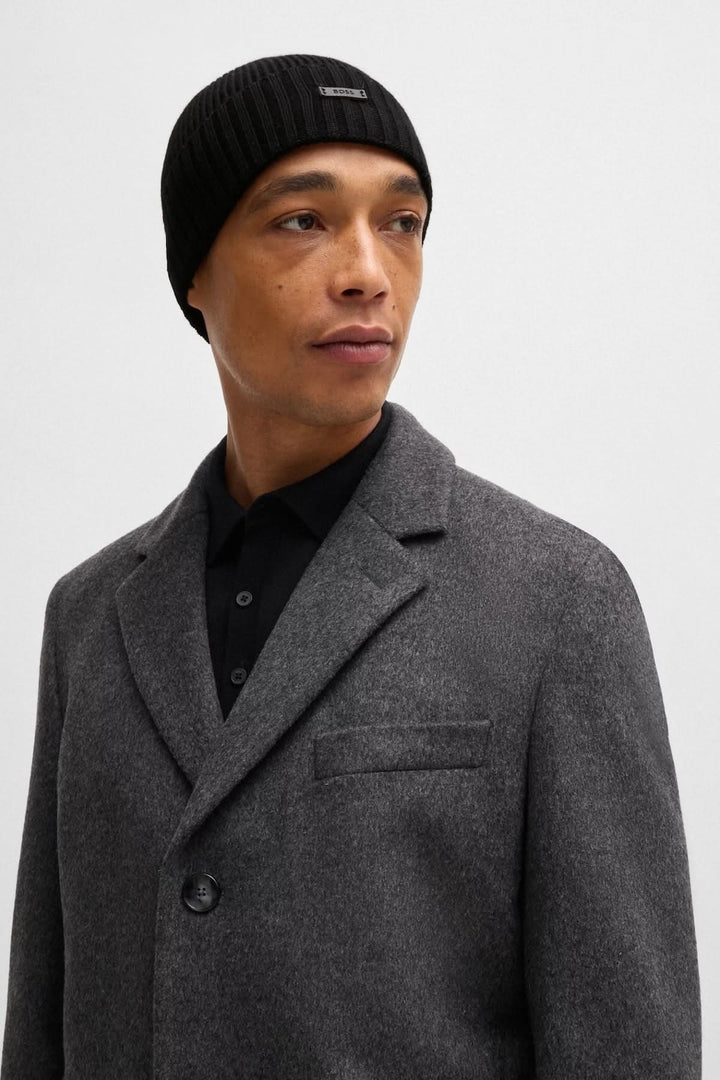 Homme portant une tuque de laine noire avec un manteau en laine gris et une chemise noire.