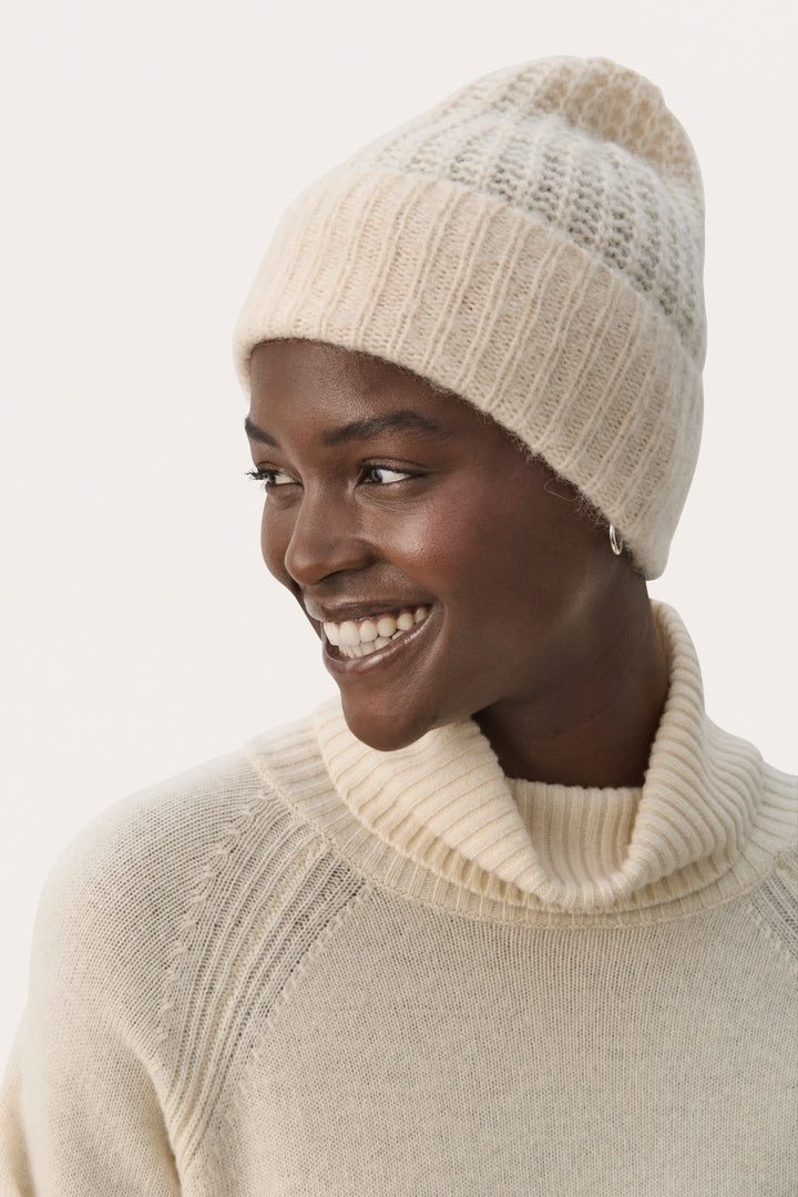 Femme souriante portant une tuque moelleuse beige et un pull à col roulé, parfaite pour les journées froides.