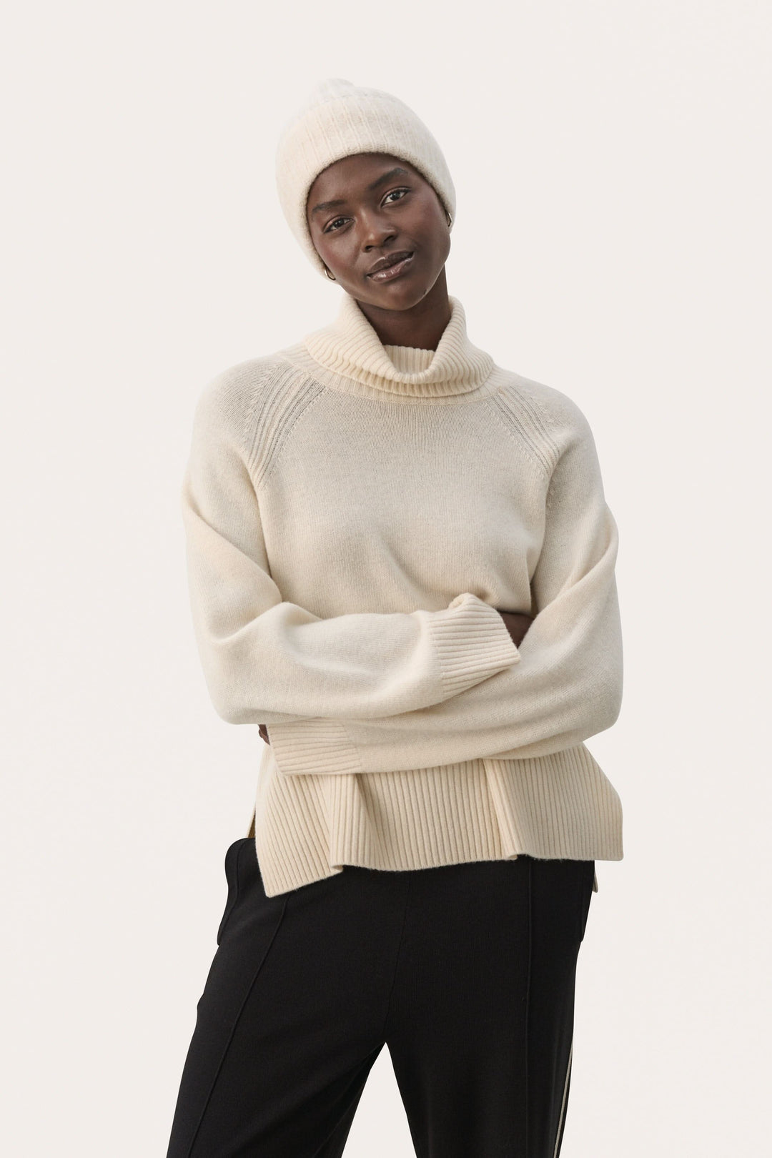 Femme portant un pull crème à col montant et une tuque assortie, dégageant une allure moderne et confortable.