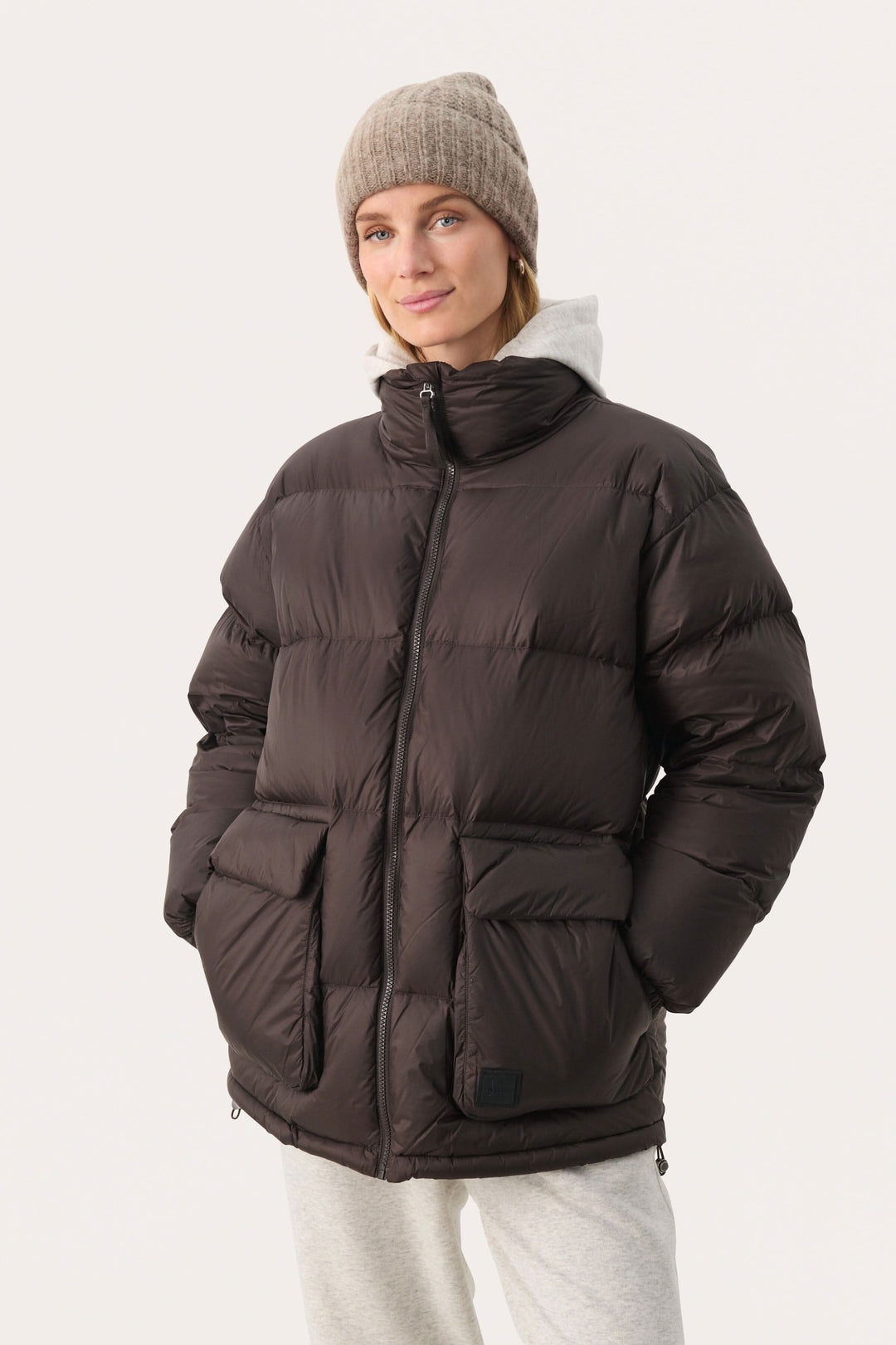 Femme souriante portant une doudoune noire avec poches et un bonnet beige, parfait pour les journées froides.