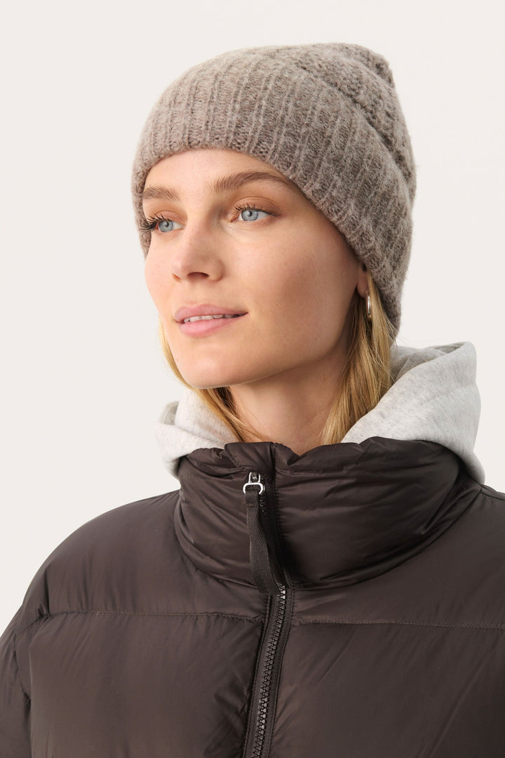 Femme portant une tuque moelleuse Micha, modèle en tricot côtelé, avec un manteau en duvet pour un look décontracté.