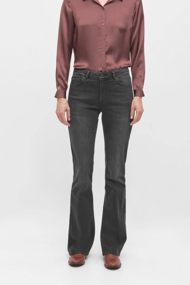 Jean noir à coupe évasée porté avec une chemise satinée, offrant un look chic et moderne.