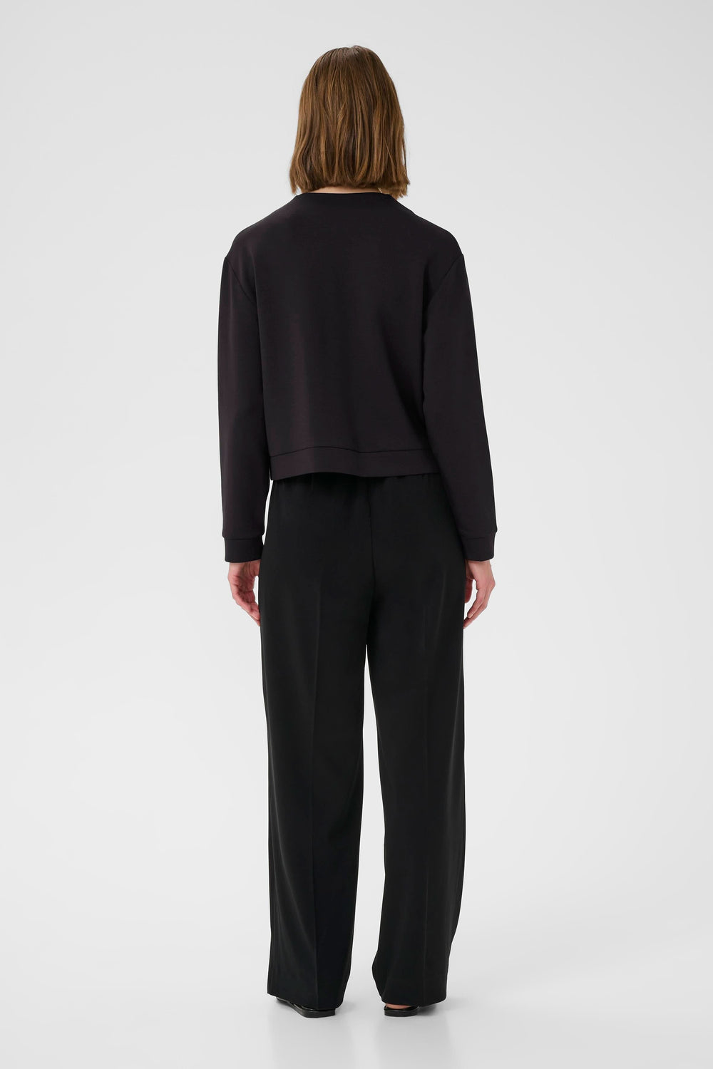Femme vue de dos portant un sweat noir avec un pantalon noir large, style décontracté et moderne.
