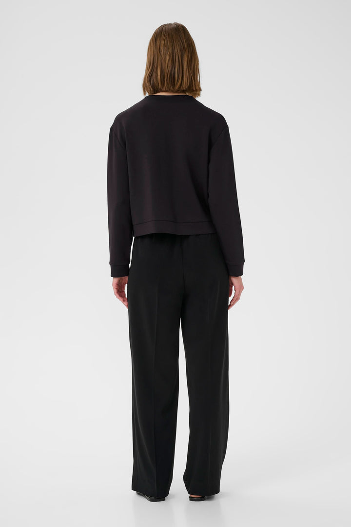 Femme vue de dos portant un sweat noir avec un pantalon noir large, style décontracté et moderne.