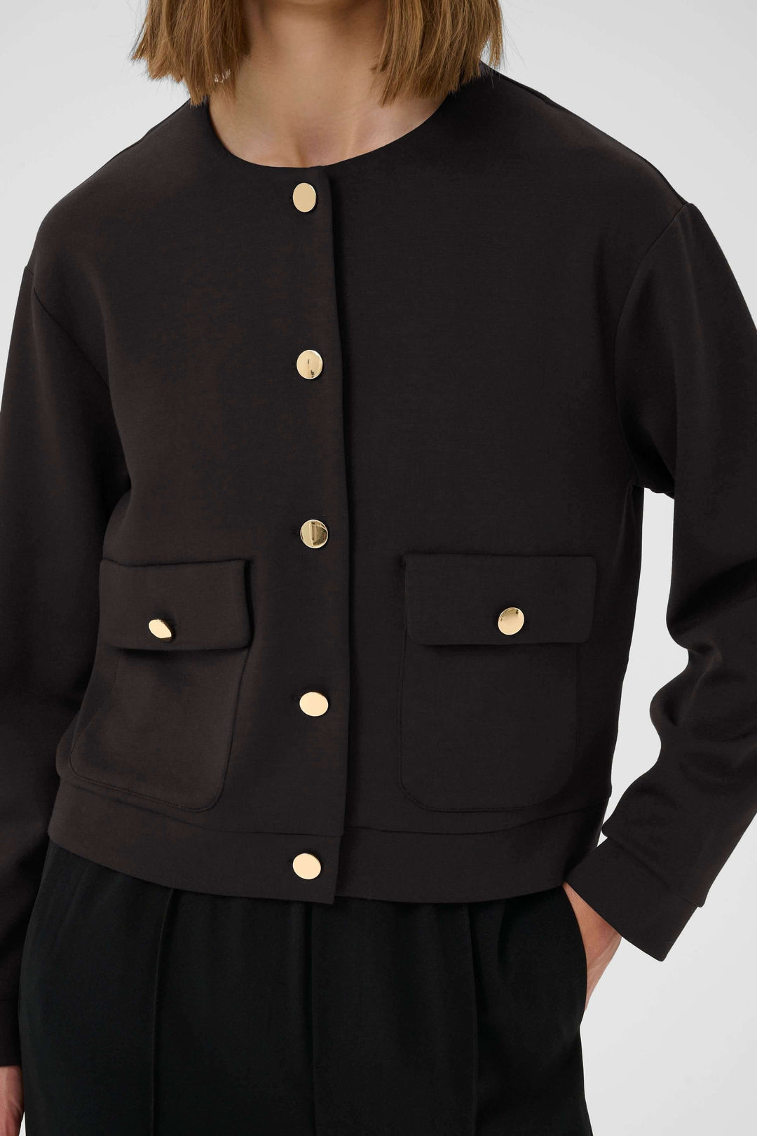 Veste Gida noire à col rond avec boutons dorés et poches, style chic et moderne.
