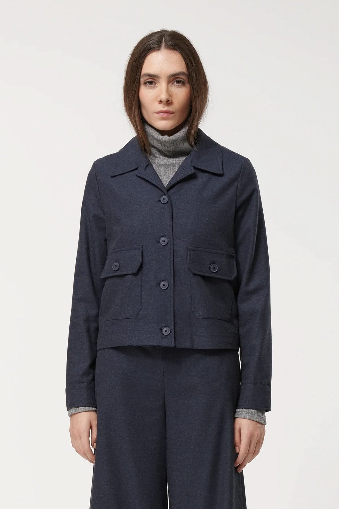 Veste Kazuko en bleu marine, coupe droite, poches à rabat, portée avec un col roulé gris.