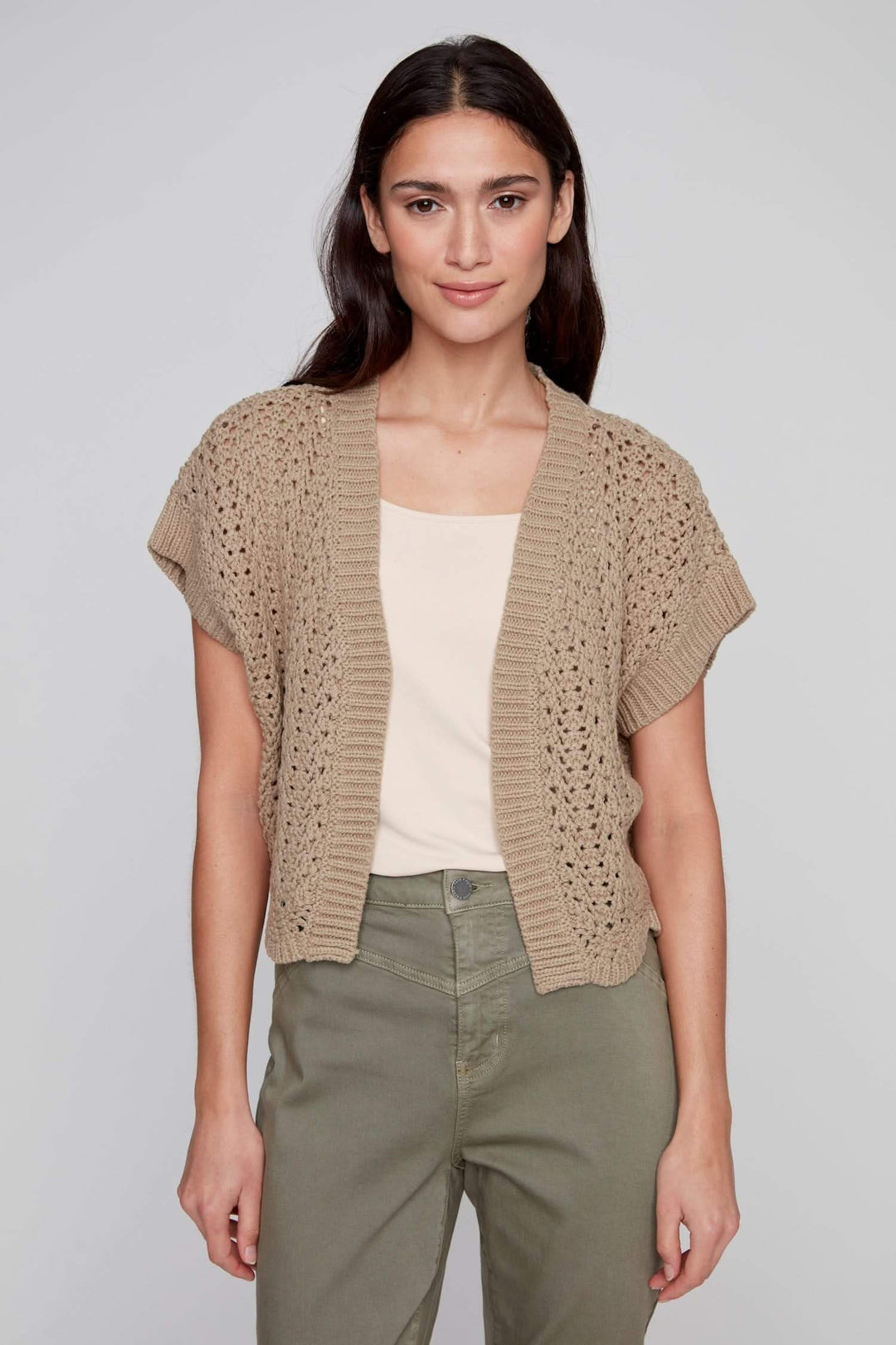 Veste au crochet beige avec manches courtes, portée sur un débardeur pour un look d'été élégant et léger.