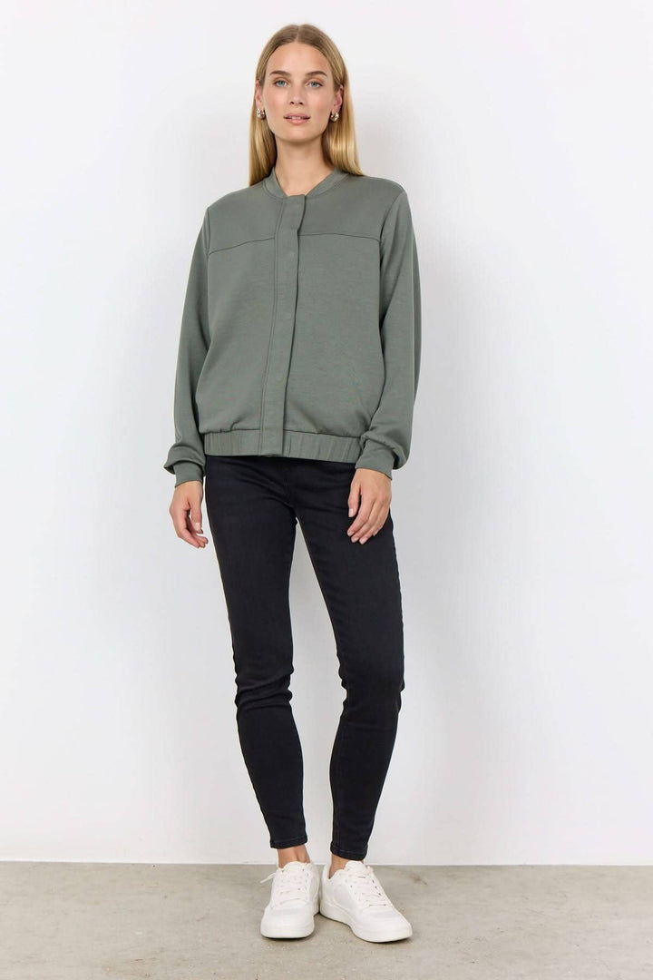Veste à bouton-pression verte portée avec un pantalon noir et des baskets blanches, affichant un style chic et décontracté.