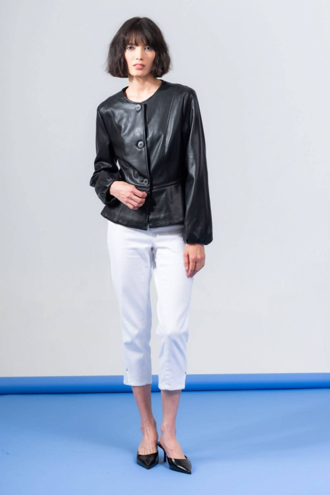 Veste péplum boutonnée en PU noire portée avec un pantalon blanc, affichant un style chic et moderne.