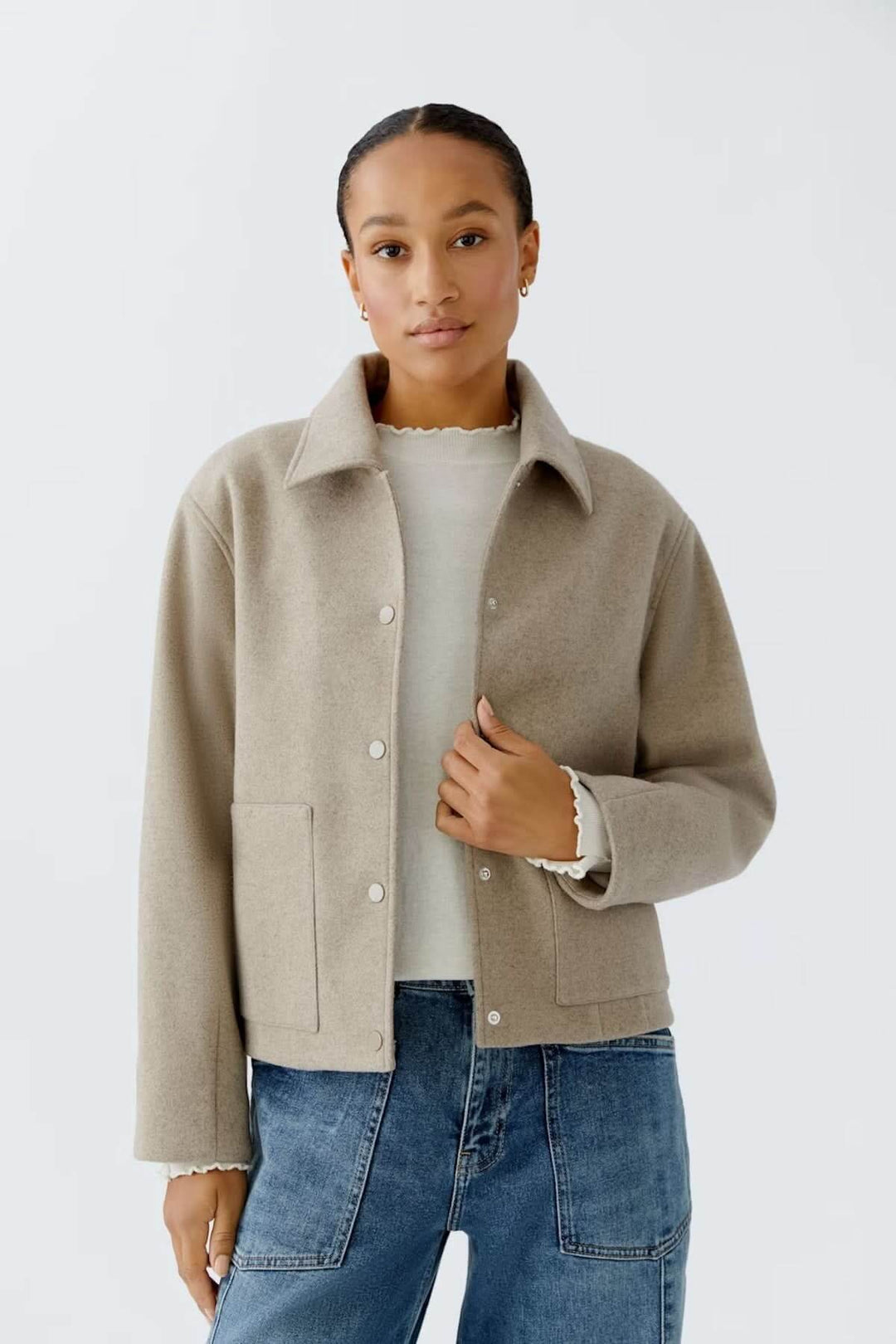 Veste à coupe droite beige avec col classique et boutons-pression, portée par modèle sur un chandail fin et jean pour un look casual chic.
