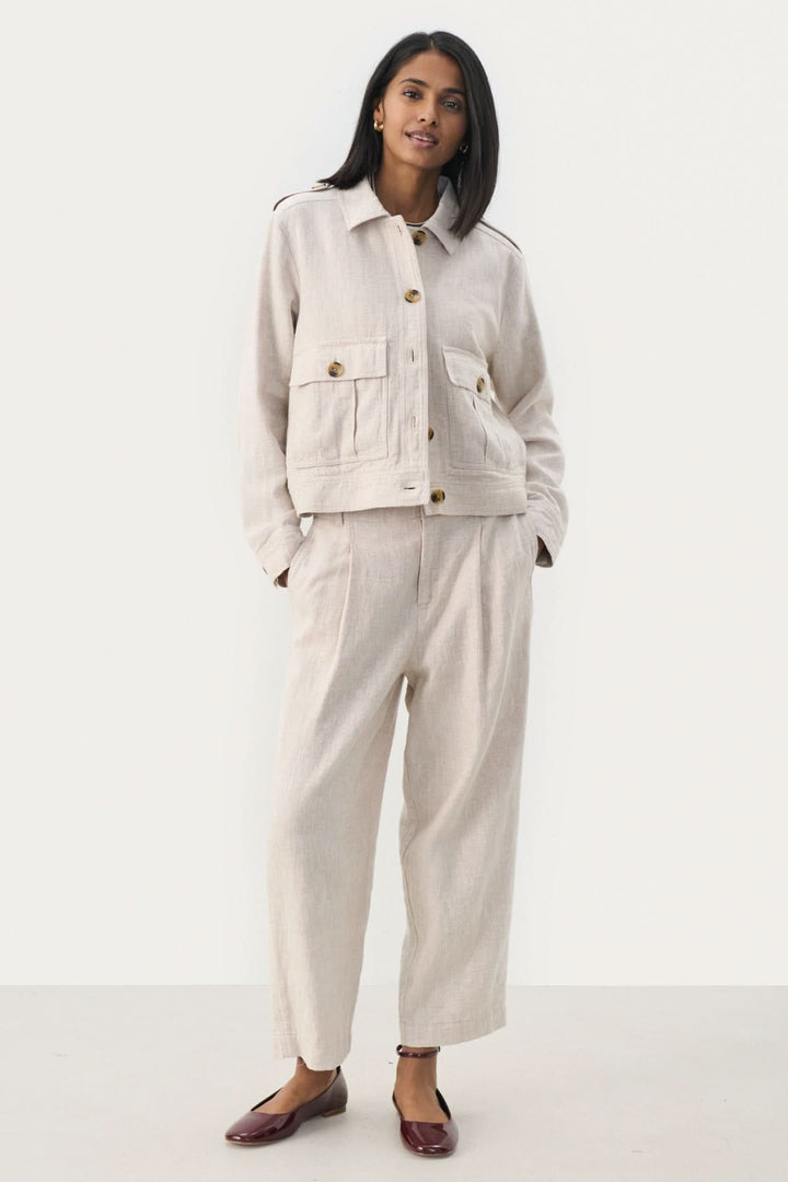 Veste courte Najah beige avec manches longues, poches avant et boutons, portée avec un pantalon assorti.