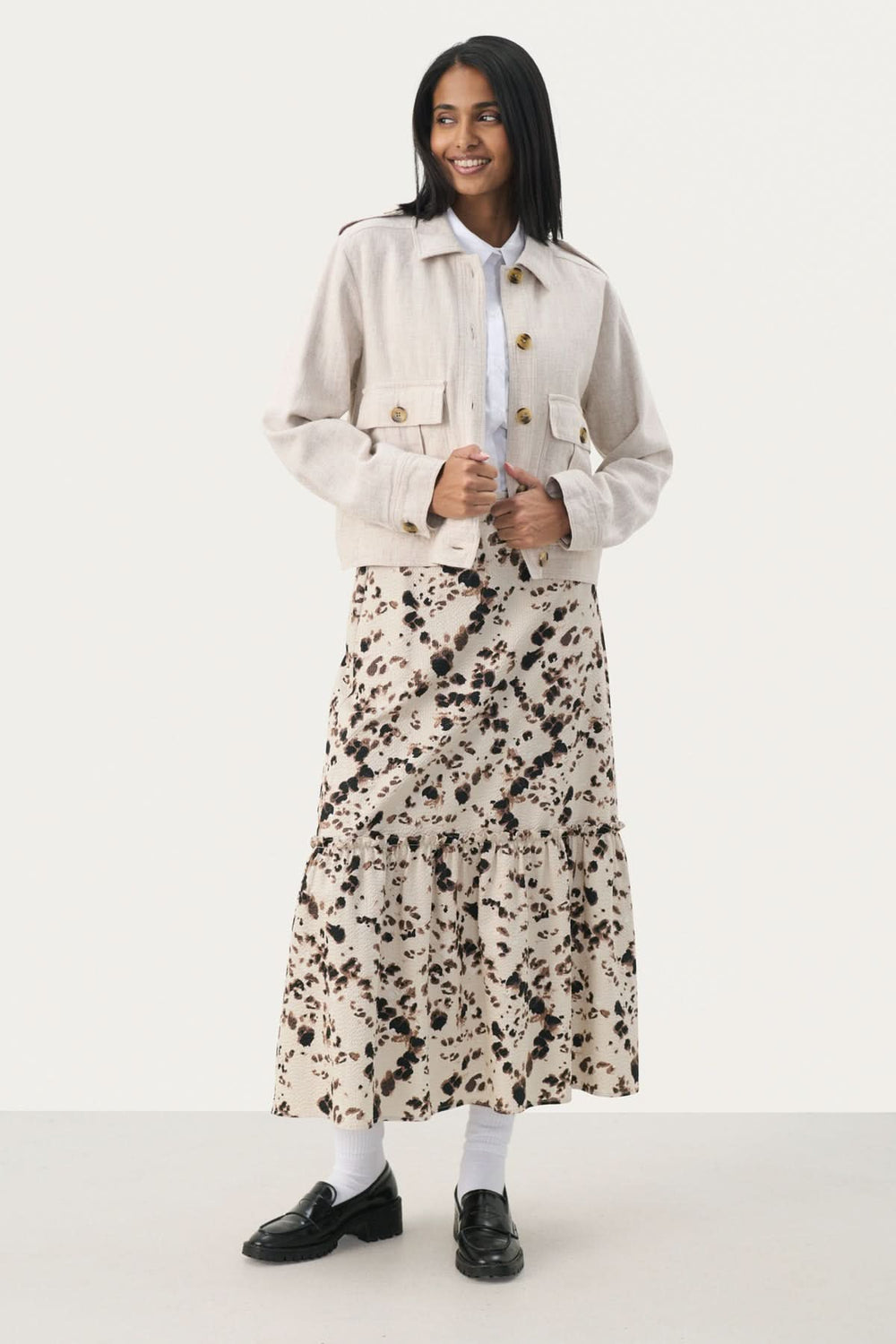 Femme portant la veste courte Najah avec une jupe fleurie, col chemise et poches avant, style élégant.