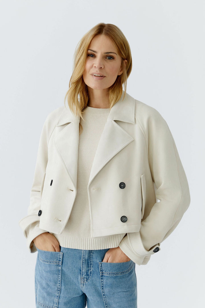 Veste courte croisée à col tailleur blanche pour un style élégant et contemporain, portée avec un pull crème et un jean casual.