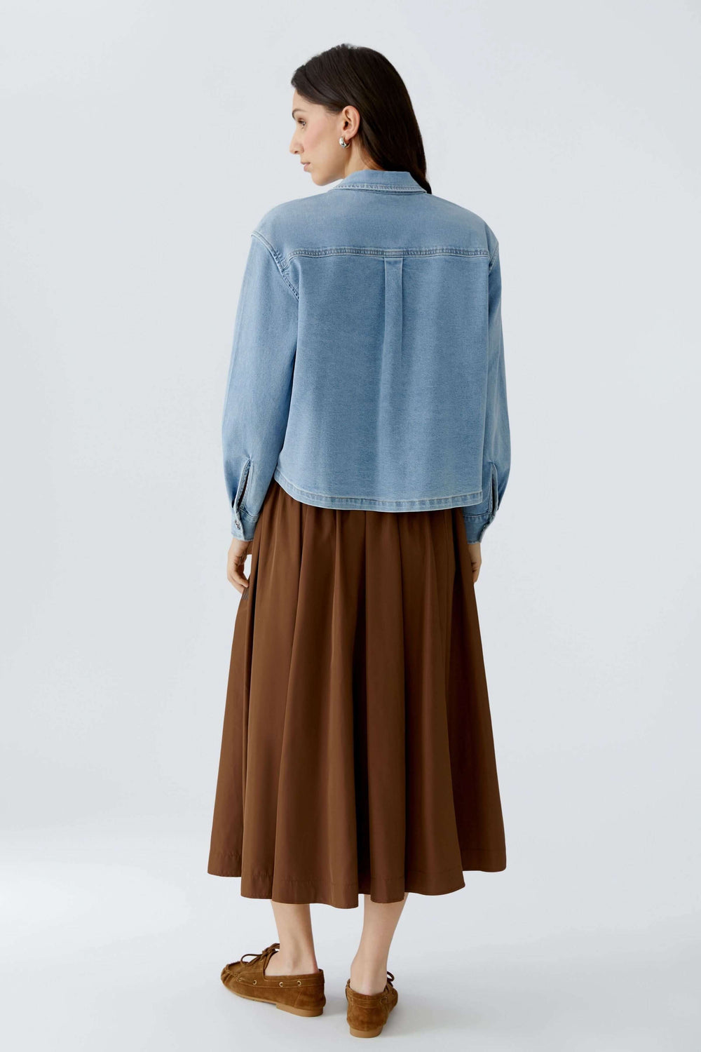 Arrière de la veste en denim sur une femme portant une jupe marron, montrant une coupe droite et ample pour une allure moderne.