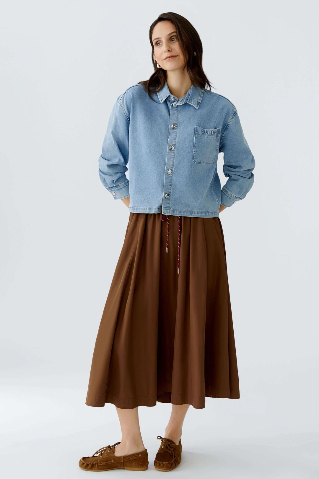 Veste en denim décontractée et moderne, coupe droite légèrement ample, longueur raccourcie, portée avec une jupe marron.