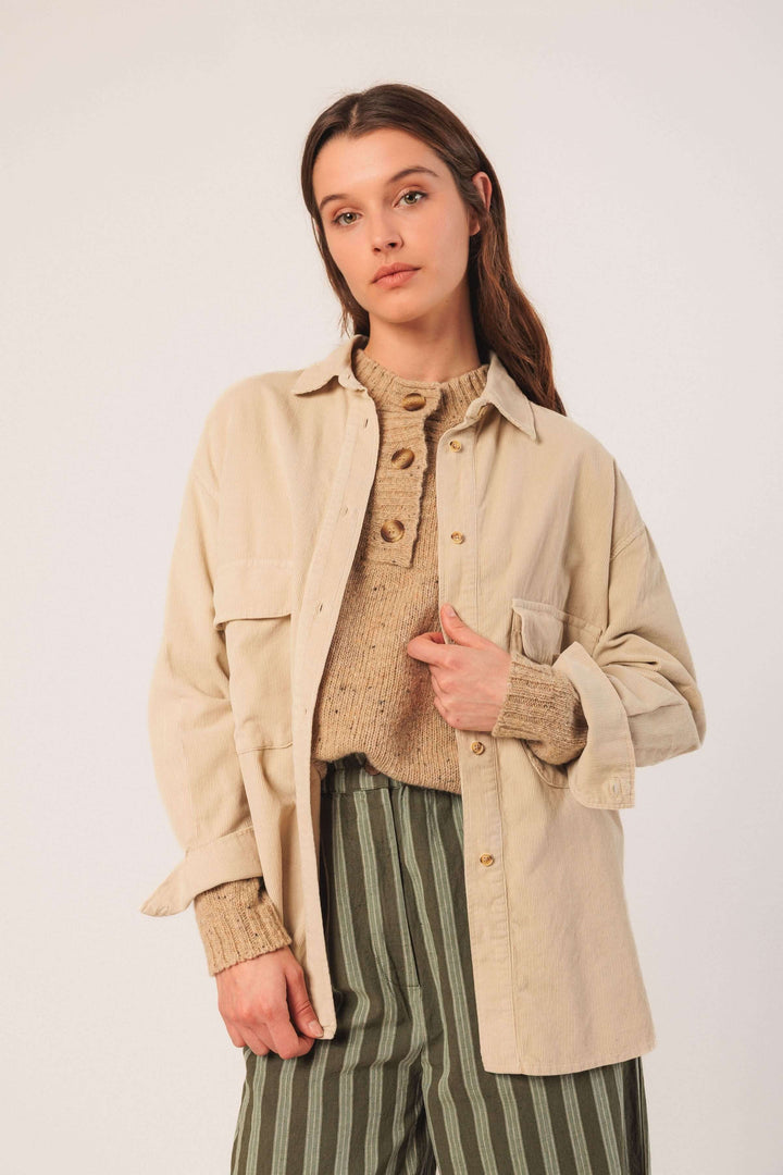 Femme portant une veste en velours côtelé beige avec un chandail et un pantalon à rayures, style décontracté.