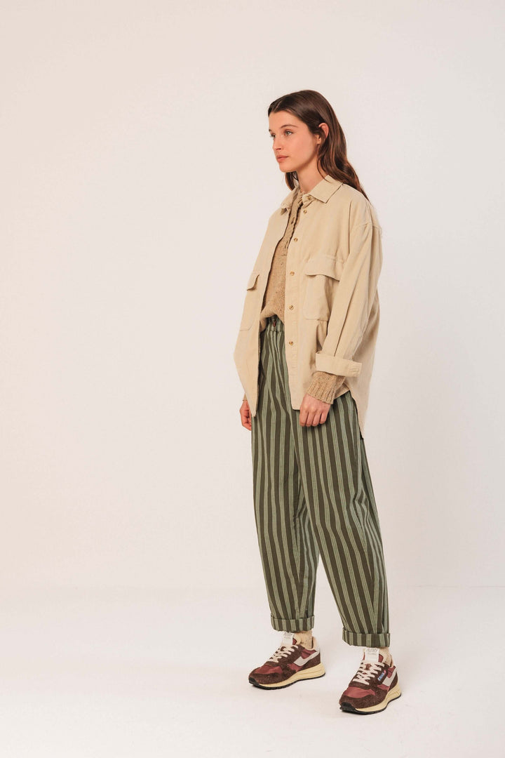 Femme portant une veste en velours côtelé beige, pantalon rayé vert, et chaussures décontractées, style moderne.