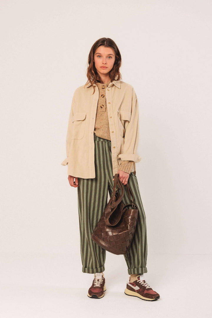 Femme portant une veste en velours côtelé beige, un pull beige, et un pantalon rayé vert avec un sac en cuir.