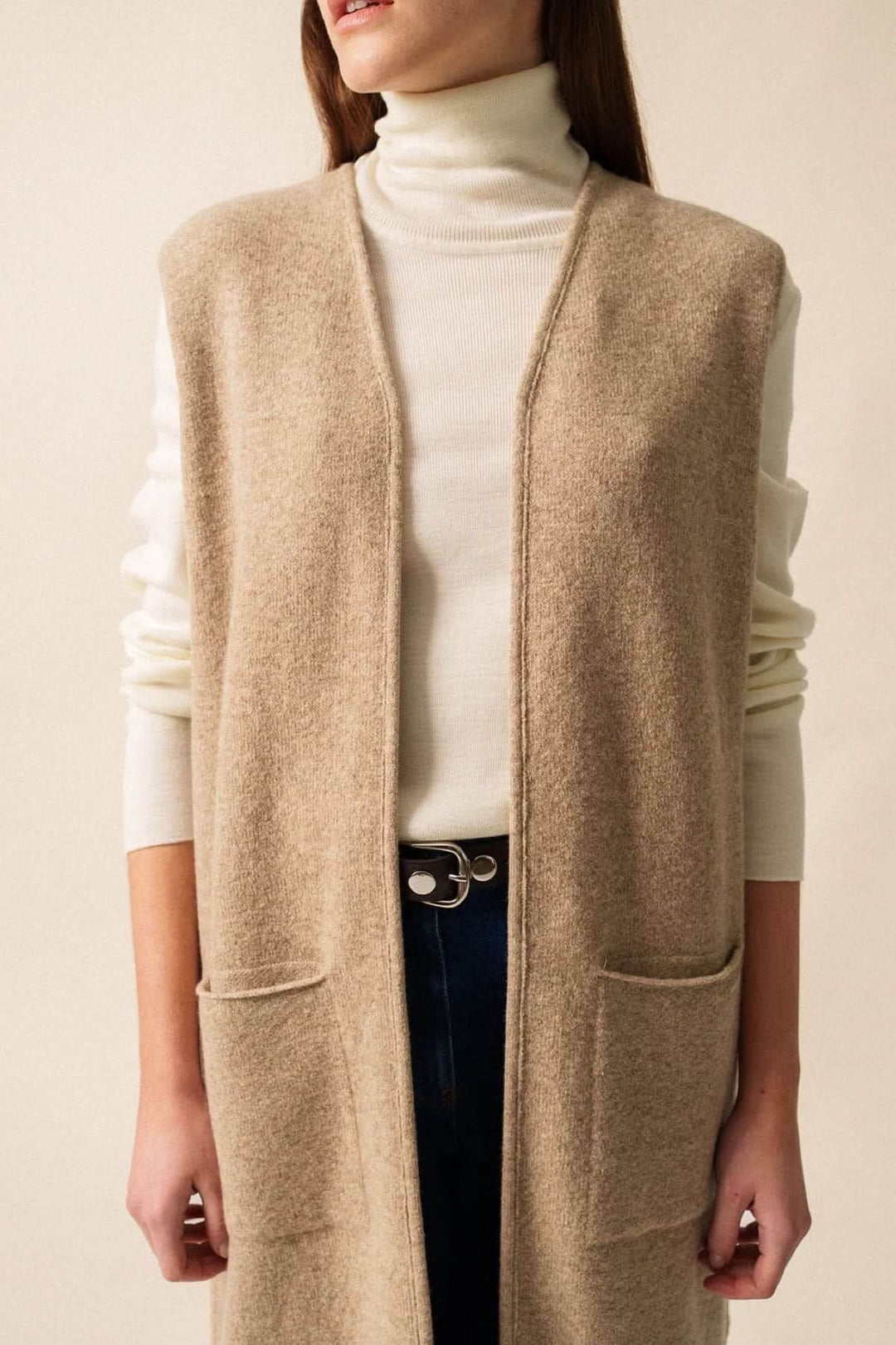 Veste longue sans manches en maille beige avec poches, idéale pour un look moderne et cosy.