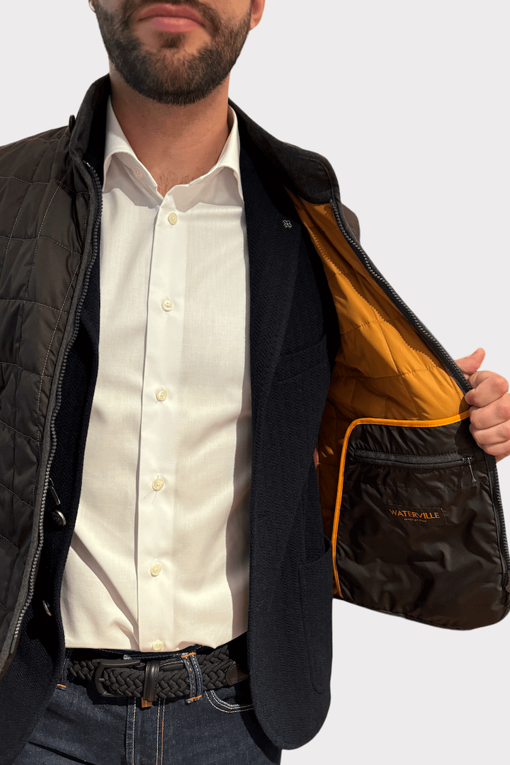 Veste matelassée en nylon noire, légère, avec doublure orange, portée par un homme en chemise blanche.