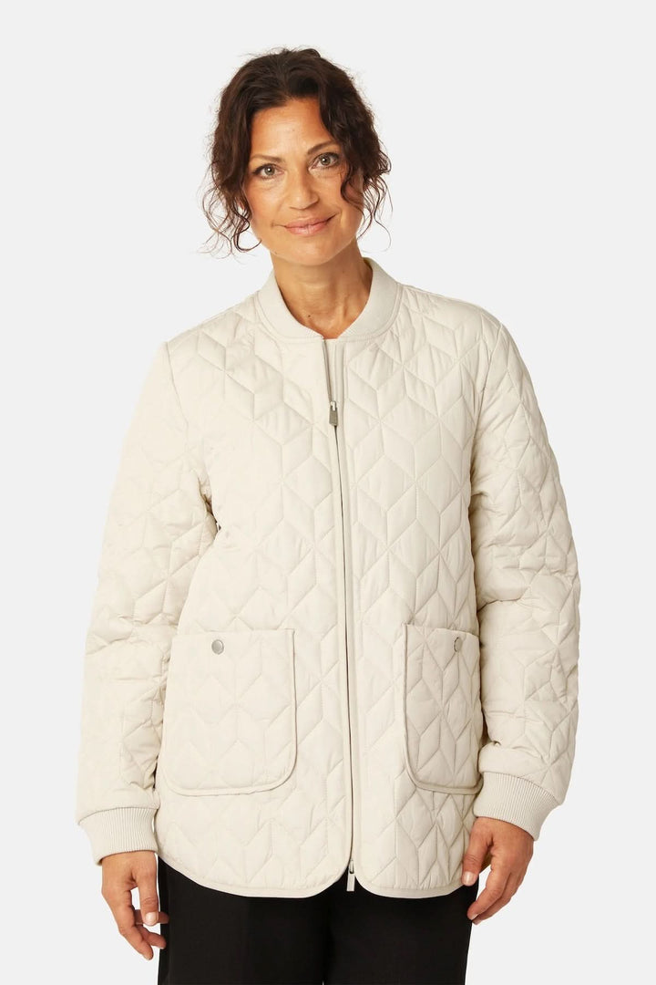 Femme portant une veste matelassée mi-longue à fermeture éclair avec poches plaquées, en couleur crème.