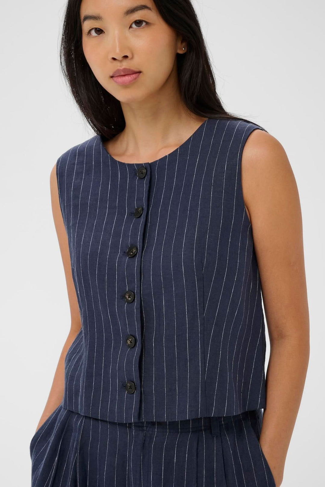 Modèle portant une Veste sans manches Azania avec motif rayé vertical et fermeture boutonnée pour un look moderne et élégant.