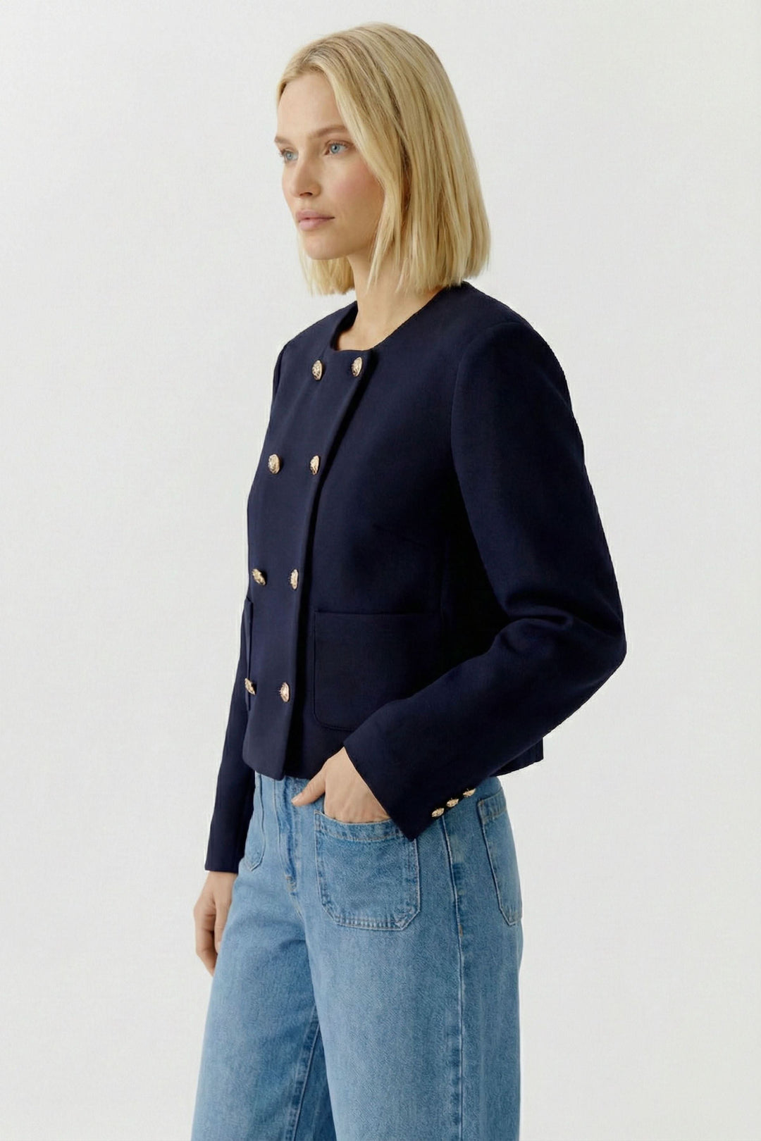 Femme portant une veste structurée à boutons décoratifs, coupe droite, style élégant, avec un jean, rehaussant un look décontracté.