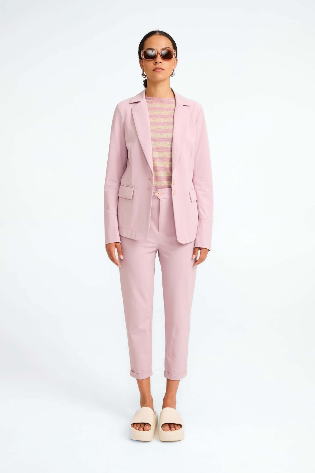 Veston Amsterdam structuré en rose, porté avec un haut rayé et un pantalon coordonné pour un look moderne et élégant.