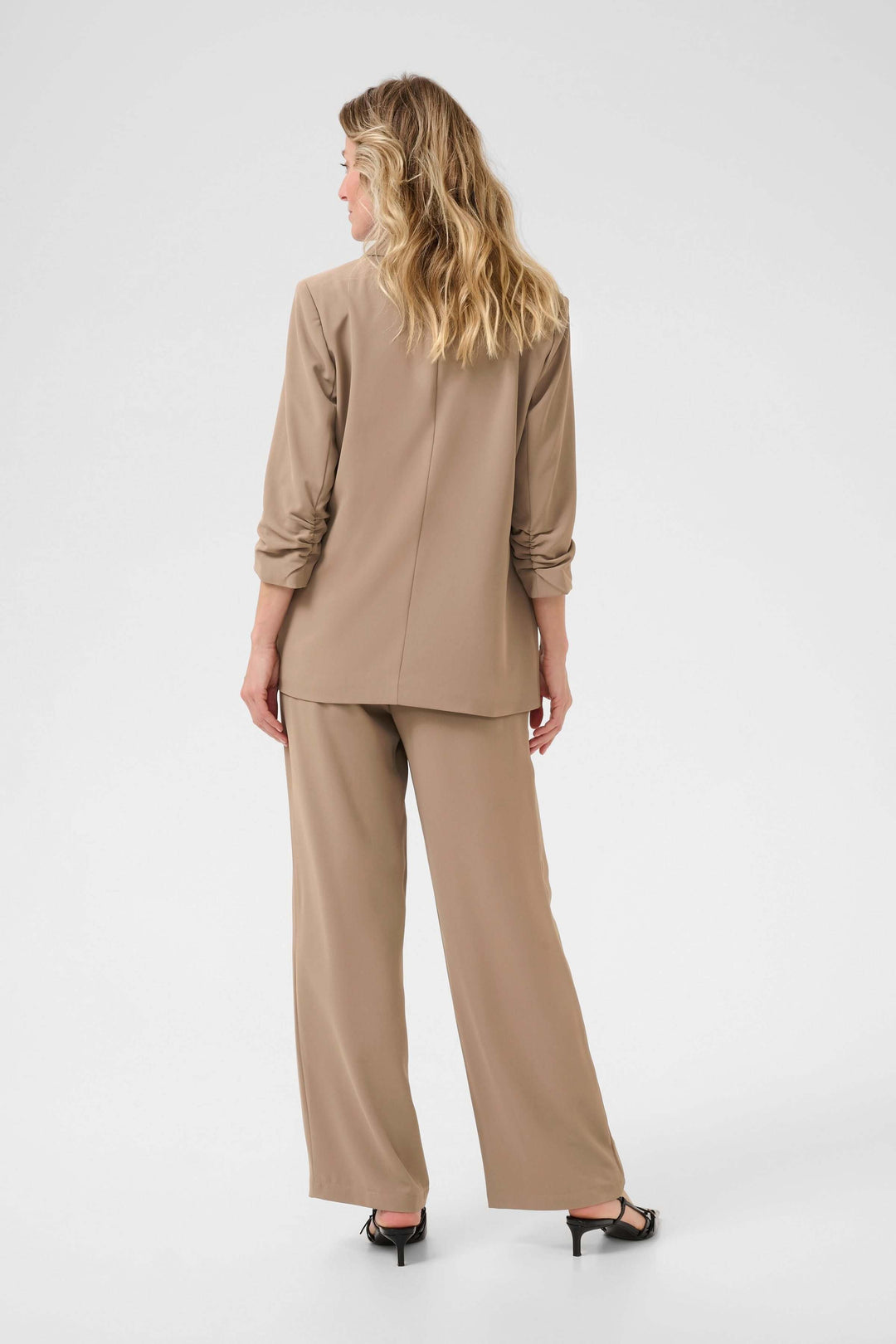 Femme vue de dos portant un veston décontracté en tissu souple avec pantalons assortis, couleur beige.